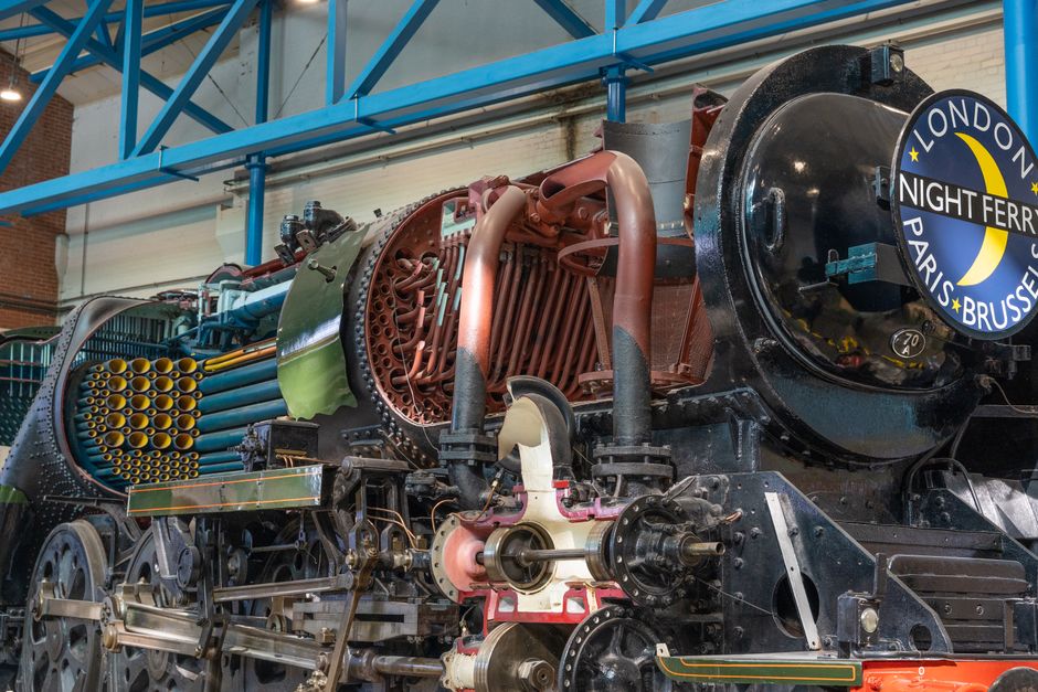 Intricate components of a vintage steam locomotive showcased indoors at a museum.